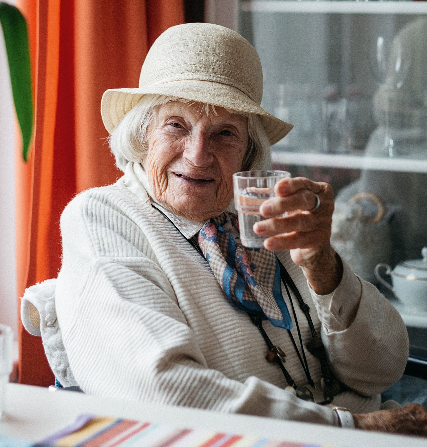 Eine Seniorin in einer Einrichtung der Seniorenpflege in Travemünde prostet mit einem Glas zu.
