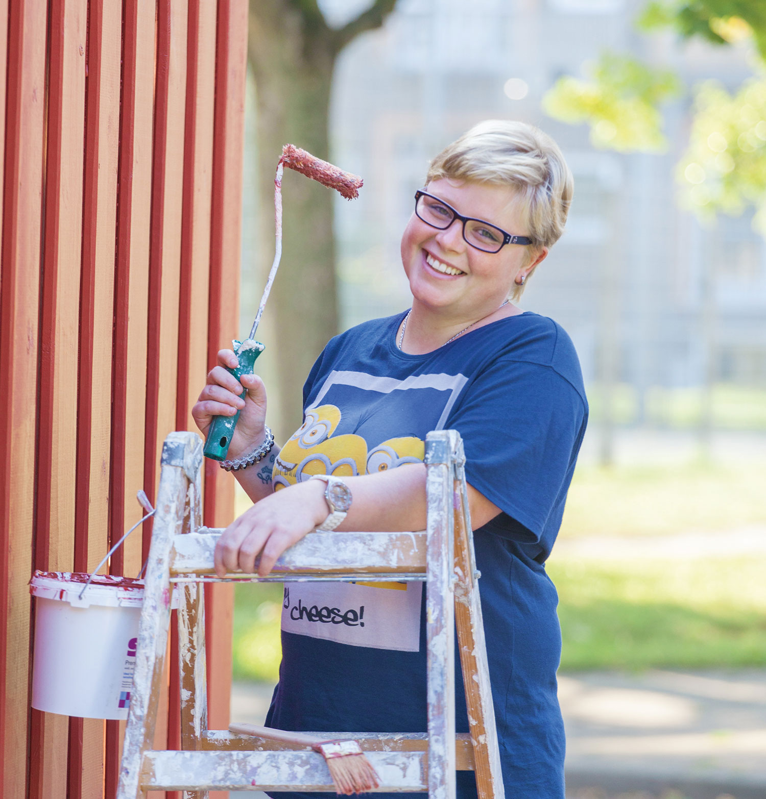 Eine Malerin steht auf einer Leiter und lächelt in die Kamera.