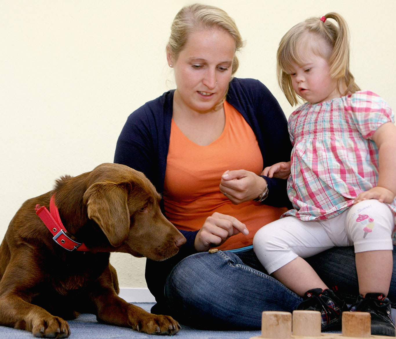 Ein Mädchen gibt einem Hund mit Hilfe einer Frühförderin ein Leckerli.